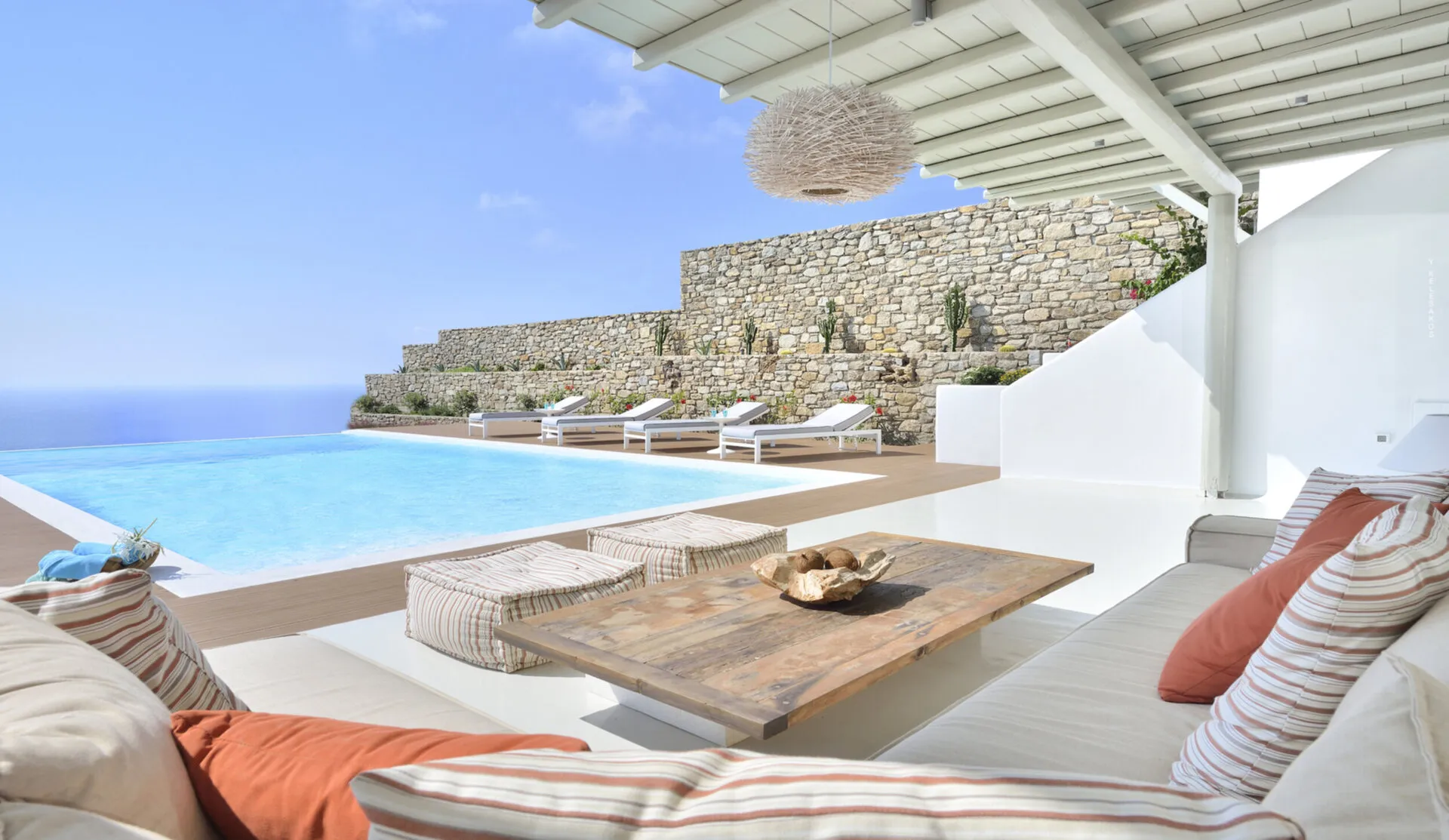 Sun-lit luxury villa in Greece perched on a cliff, overlooking sapphire Aegean waters.